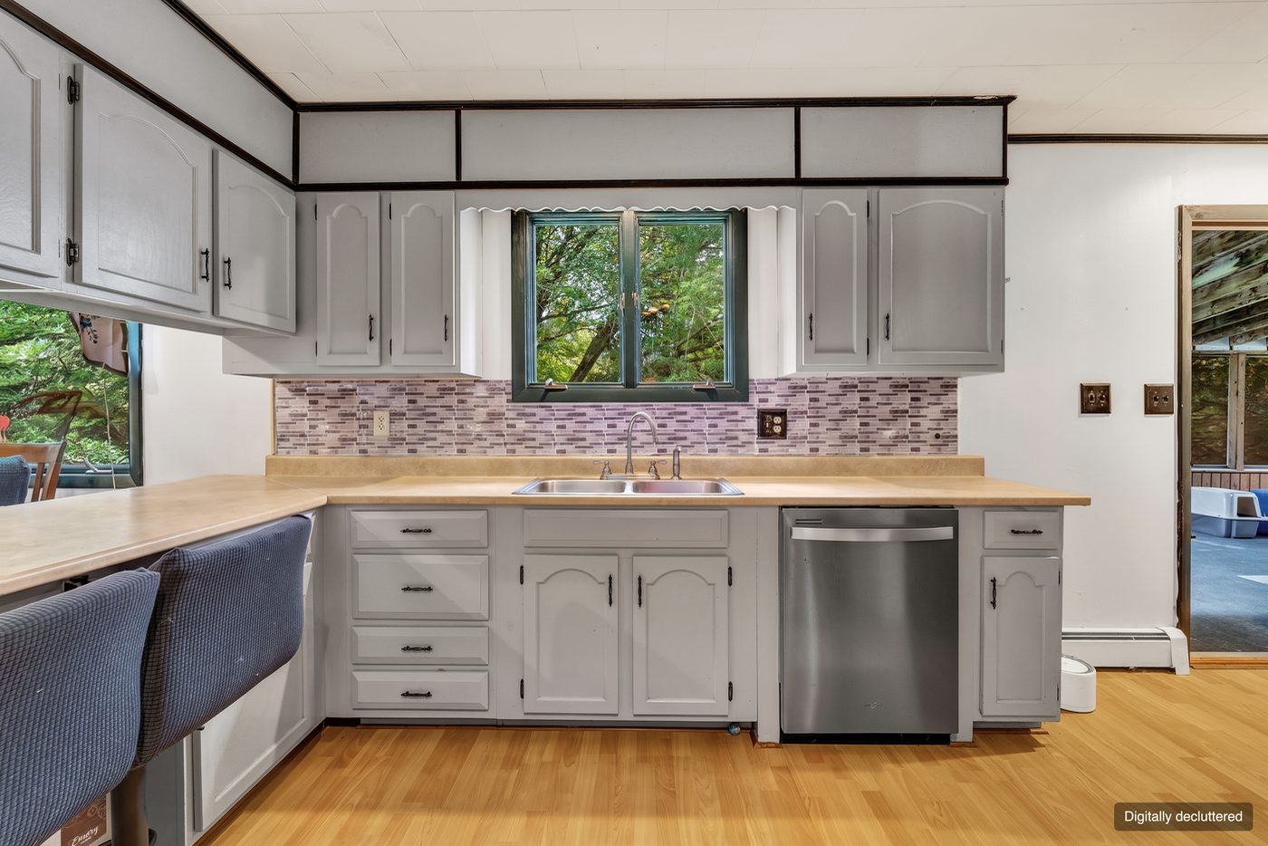 The same kitchen with the clutter gone. The cabinets, the tiled backsplash, the window and the floor are unchanged.
